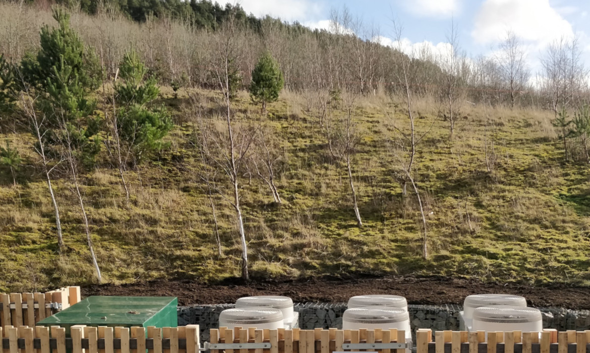view over the top of air source heat pump compound with natural hillside and forest in background